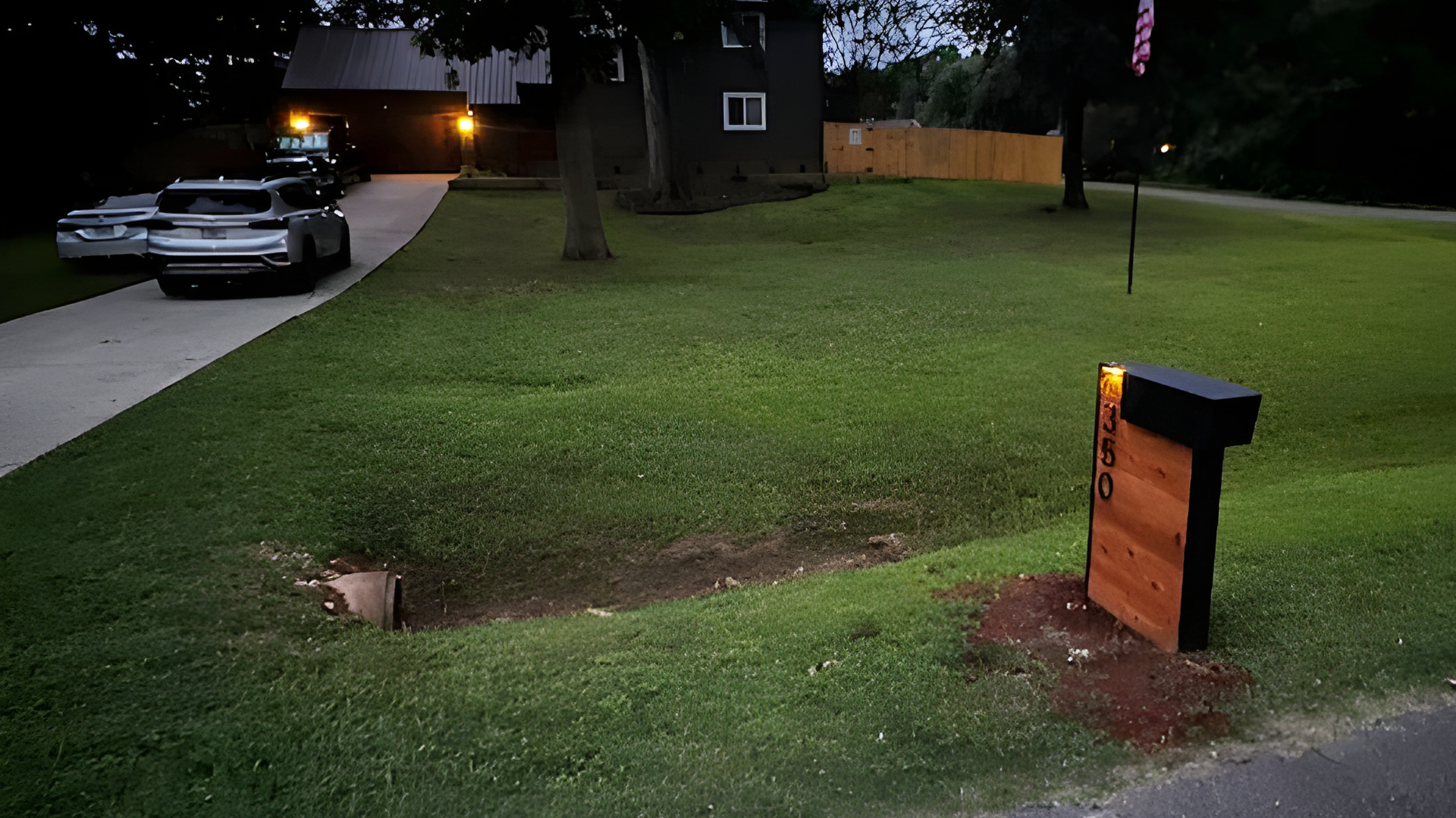 Cedar Wooden Mailbox Post on a grassy lawn at night with a house and cars in the background
