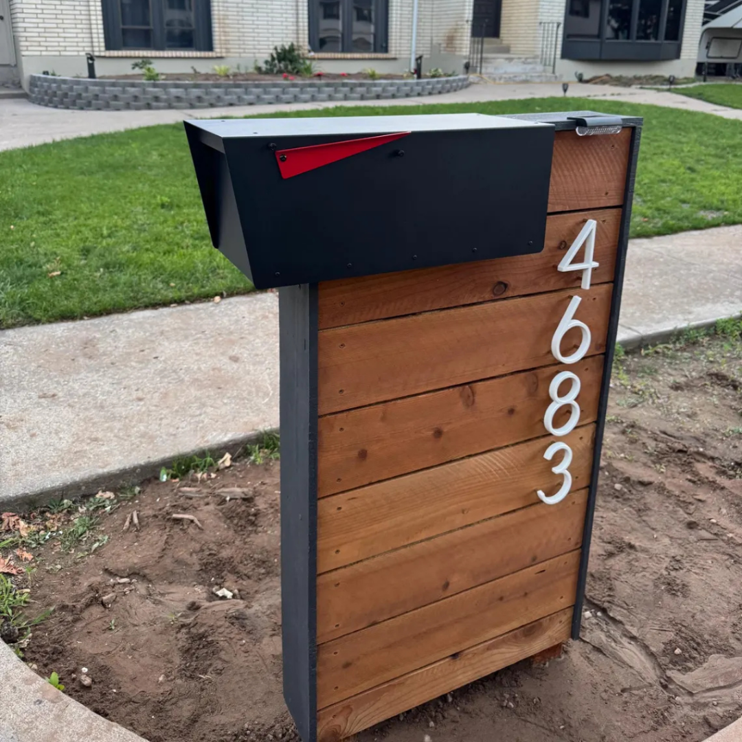 Wooden mailbox post with black steel mailbox and house numbers in front of a house